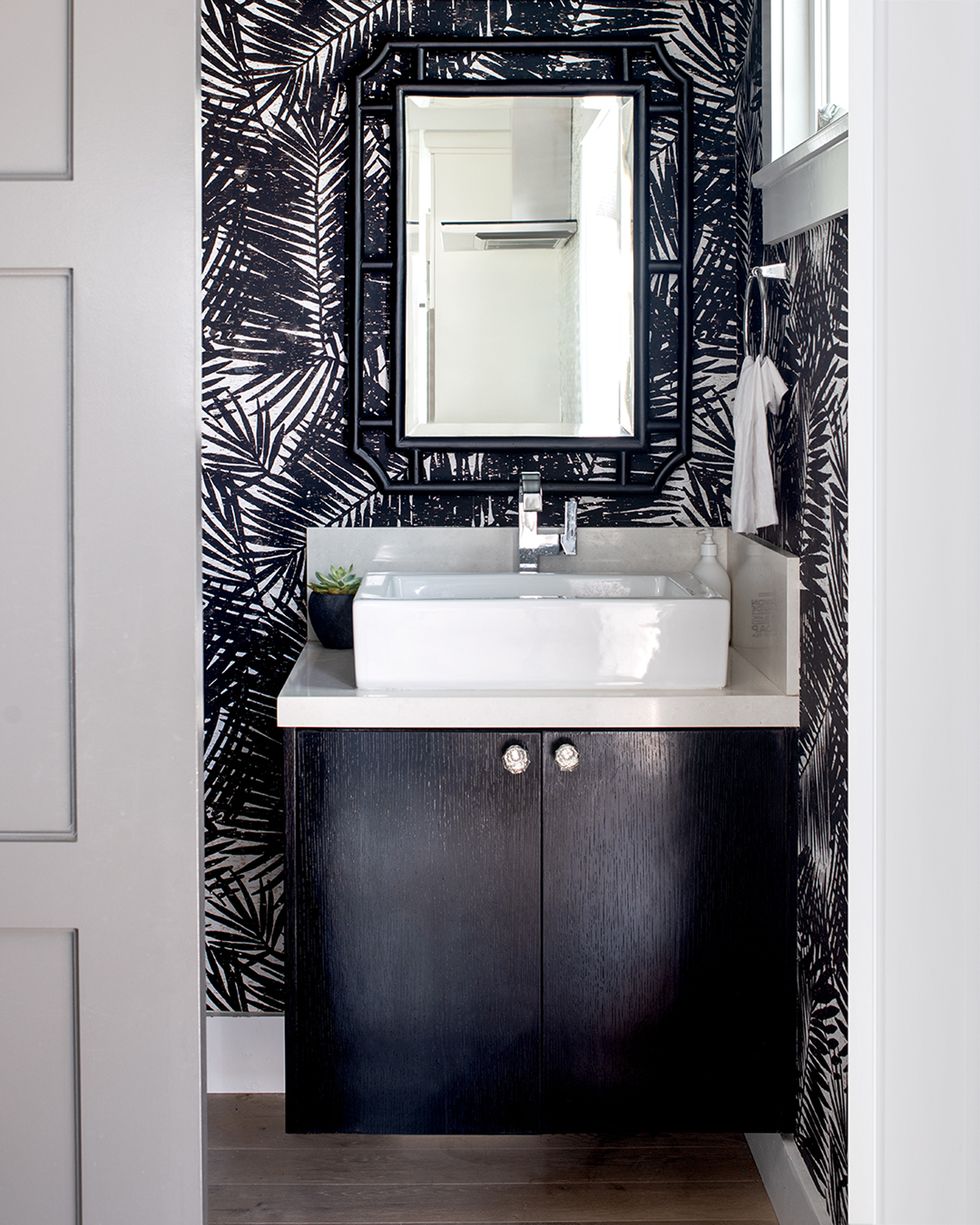 baño con mueble suspendido negro y papel pintado con motivos de hojas de palmera