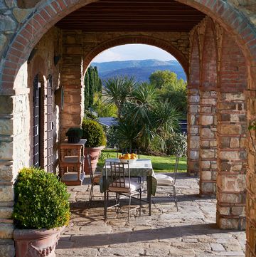 straight view through an arched loggia with table and chairs on stone looking out over the green lush tuscan countryside