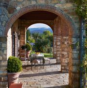straight view through an arched linnae with table and chairs on stone looking out over the green lush tuscan countryside
