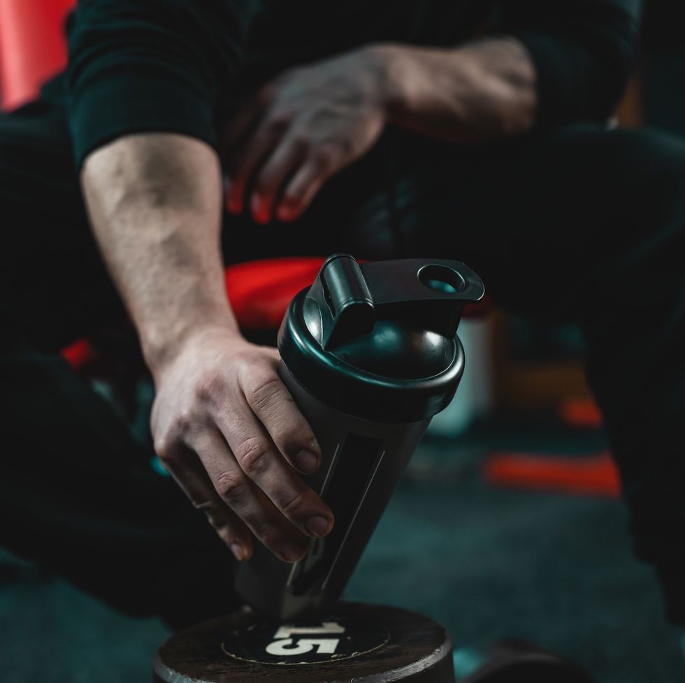 close up on hand of unknown caucasian man holding dark supplement shaker while sitting at gym during training copy space selective focus
