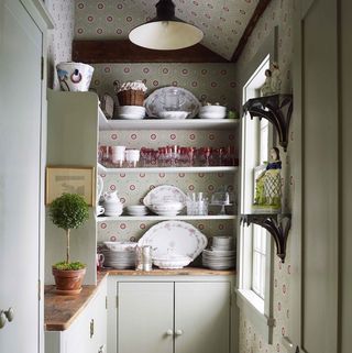 a butler’s pantry walls are covered in a recolored historic parisian pattern open shelves are filled with glasses and dishware