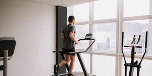 caucasian adult man running on a treadmill in the gym next to a large window