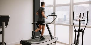 caucasian adult man running on a treadmill in the gym next to a large window