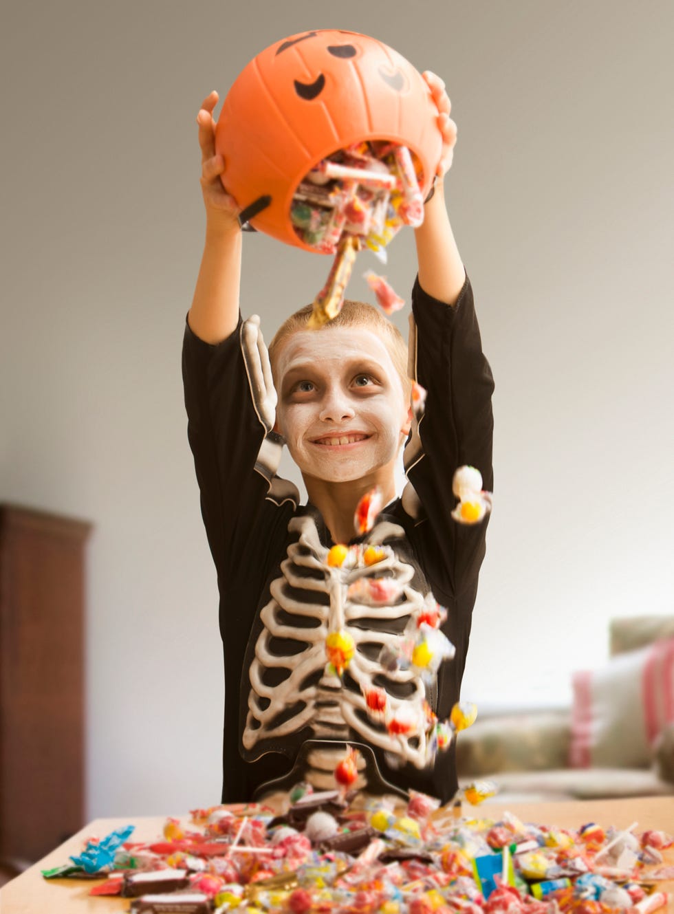 Caucasian boy in skeleton dumping out Halloween candy