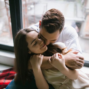 caucasian couple hugging on bench near window