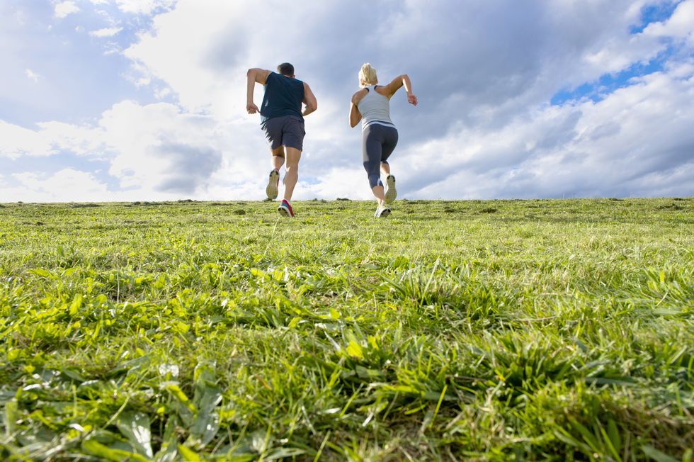 Caucasian couple jogging up grassy hill