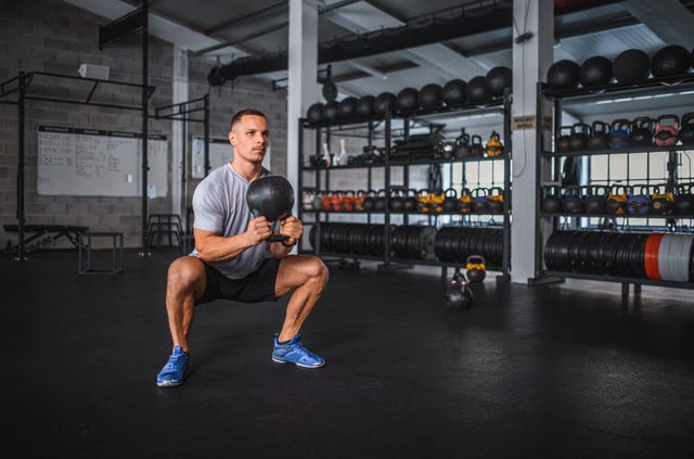 caucasian male athlete doing kettlebell sumo squat in gym