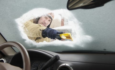 pria Kaukasia mengikis salju dari kaca depan mobil
