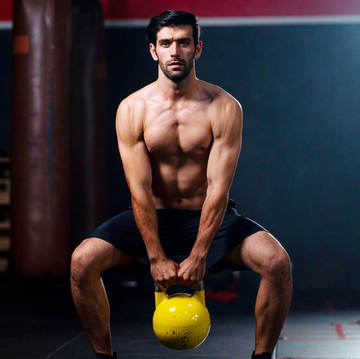 caucasian man stand with no shirt hold and pull up kettlebell in fitness gym for exercise to build up strong body and good health