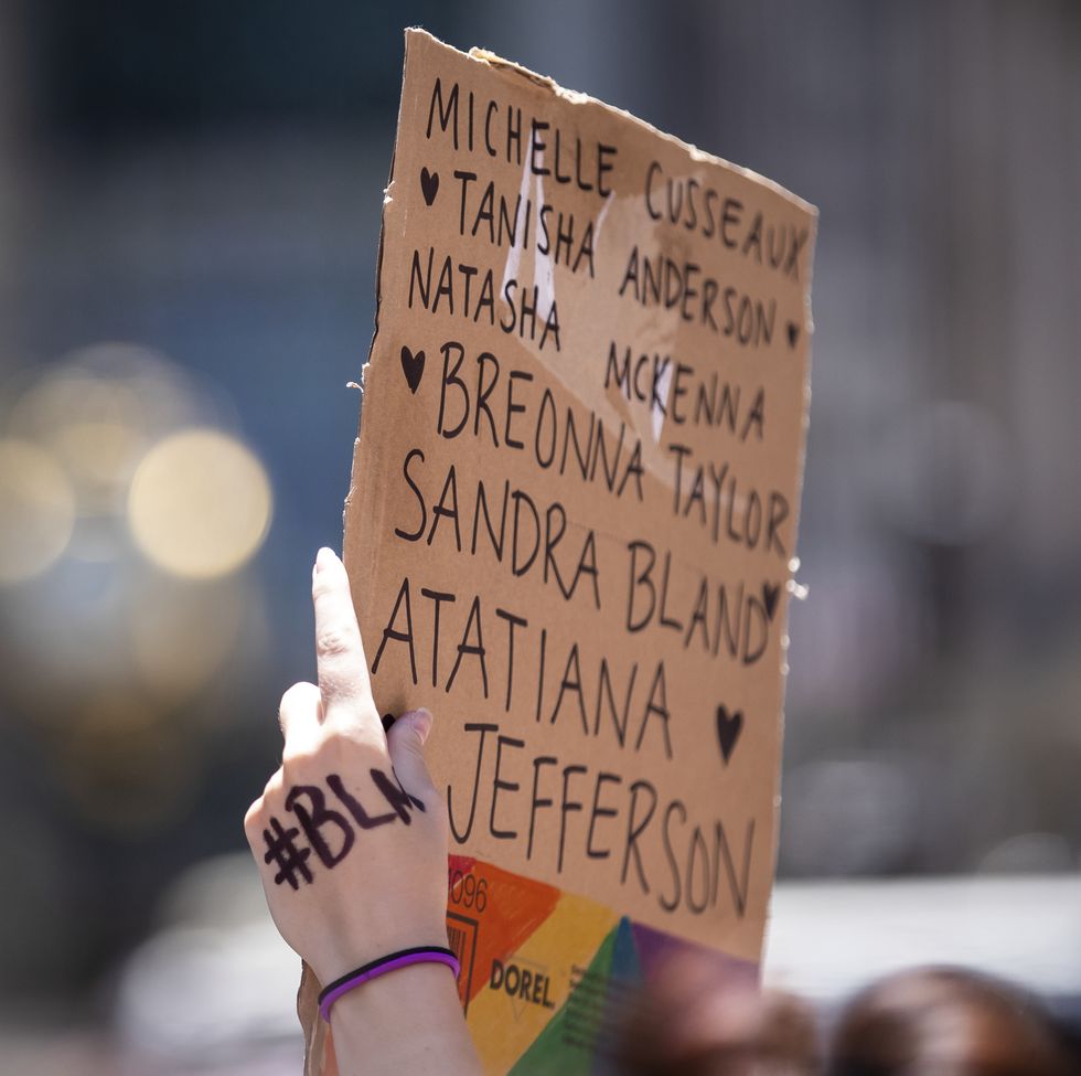 a protester holds up their homemade sign on a box that says, breonna taylor, atatiana jefferson, sandra bland natasha mckenna, tanisha anderson, michelle cusseausx with the letters blm written on their hand and the rainbow colors on the box during a protest at trump tower