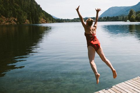 caucasian woman jumping from dock into rural lake