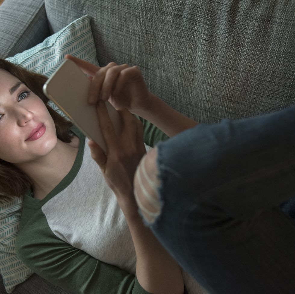 caucasian woman laying on sofa texting on cell phone
