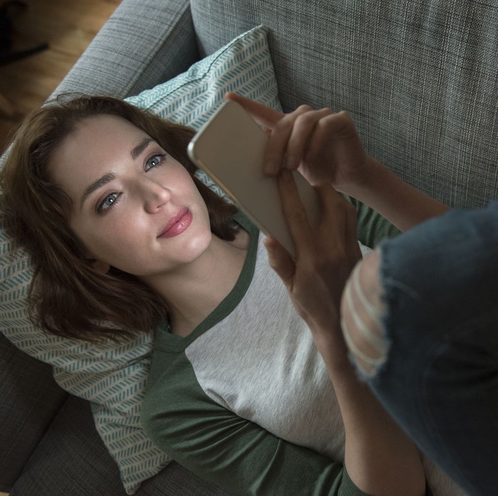 caucasian woman laying on sofa texting on cell phone
