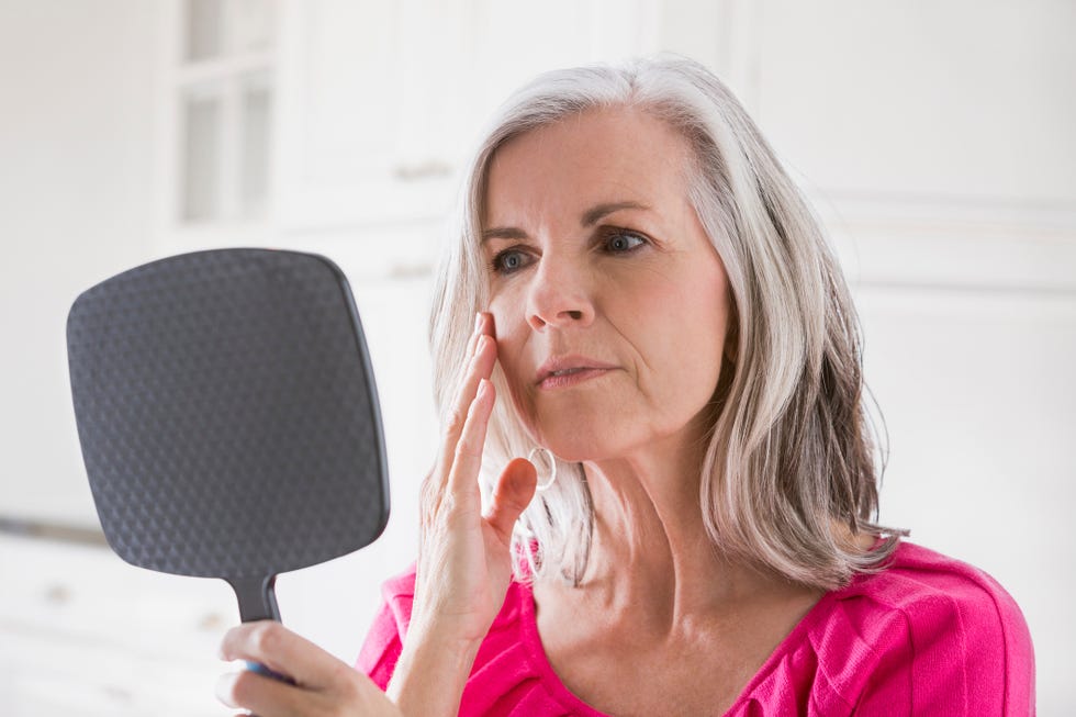 Caucasian woman looking at skin in mirror