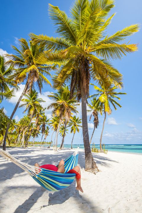 caucasian woman lying on striped hammock on a tropical beach with palm trees and white sand
