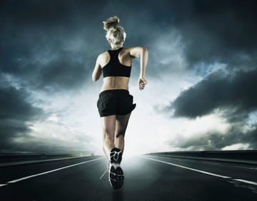 Caucasian woman running on remote road under dramatic sky