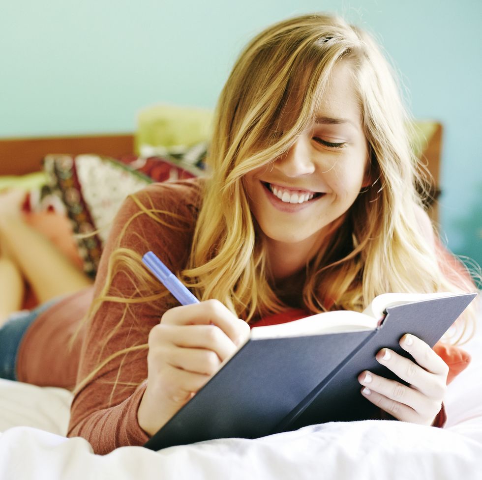 caucasian woman writing in diary on bed