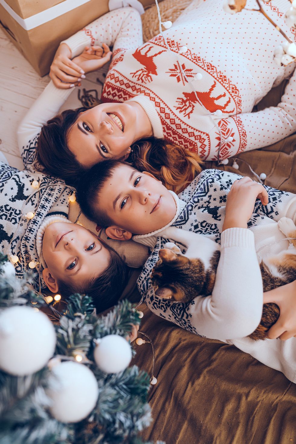 caucasian young adult mother with two sons celebrating christmas and new year at home under the christmas tree