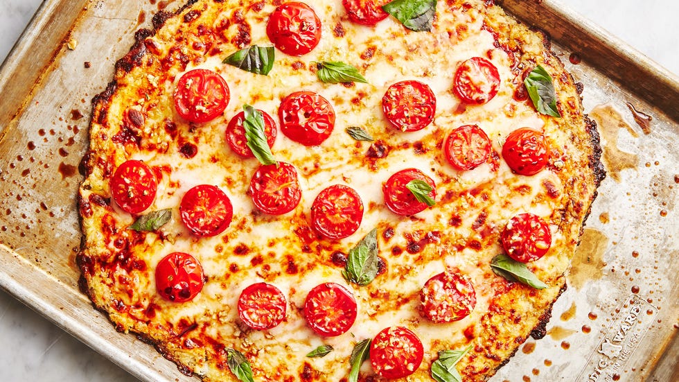 pizza crust made from riced cauliflower topped with cheese, halved tomatoes, and basil