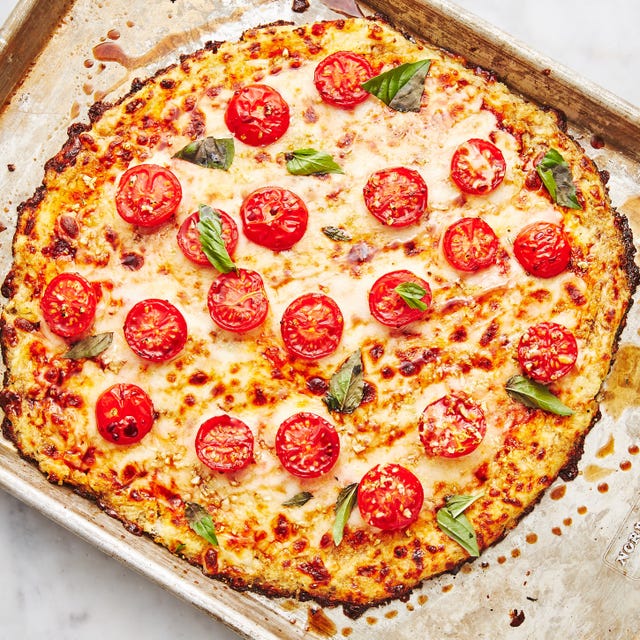 pizza crust made from riced cauliflower topped with cheese, halved tomatoes, and basil