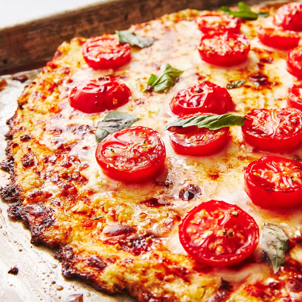 pizza crust made from riced cauliflower topped with cheese, halved tomatoes, and basil