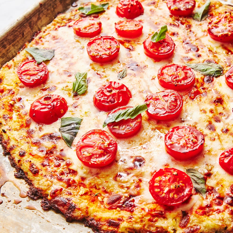 pizza crust made from riced cauliflower topped with cheese, halved tomatoes, and basil