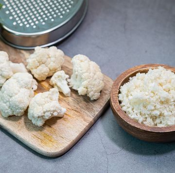 cauliflower rice on a wooden bowl with some cauliflower\'s pieces on a table in concrete background