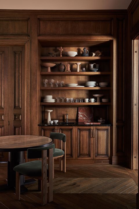 a wood paneled living room with chairs near a table and shelf full of homewares