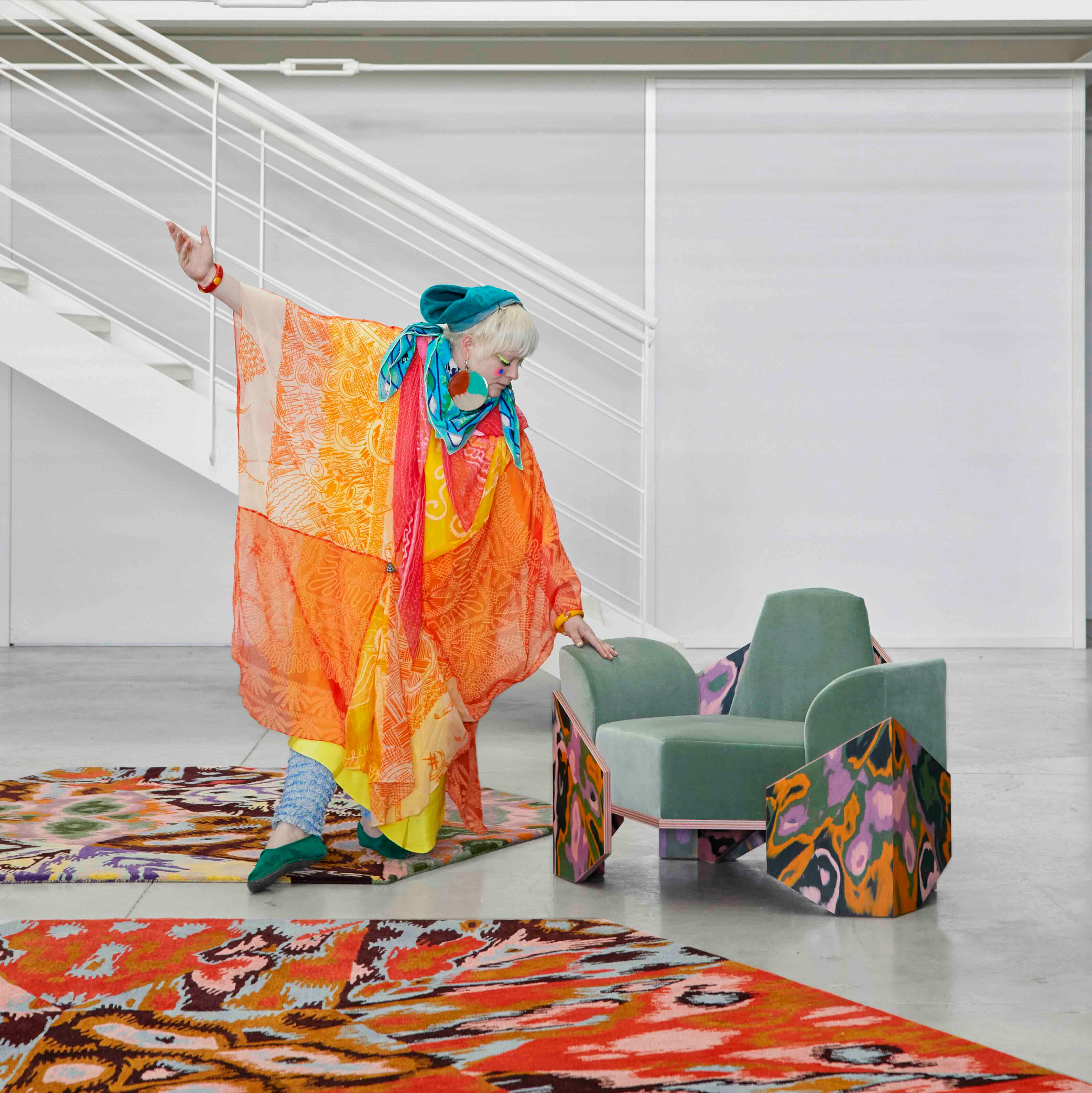 Bethan Laura Wood Ways of Seeing CC Tapis a vibrant individual dressed in colorful fashion poses with an artistic armchair in a modern space