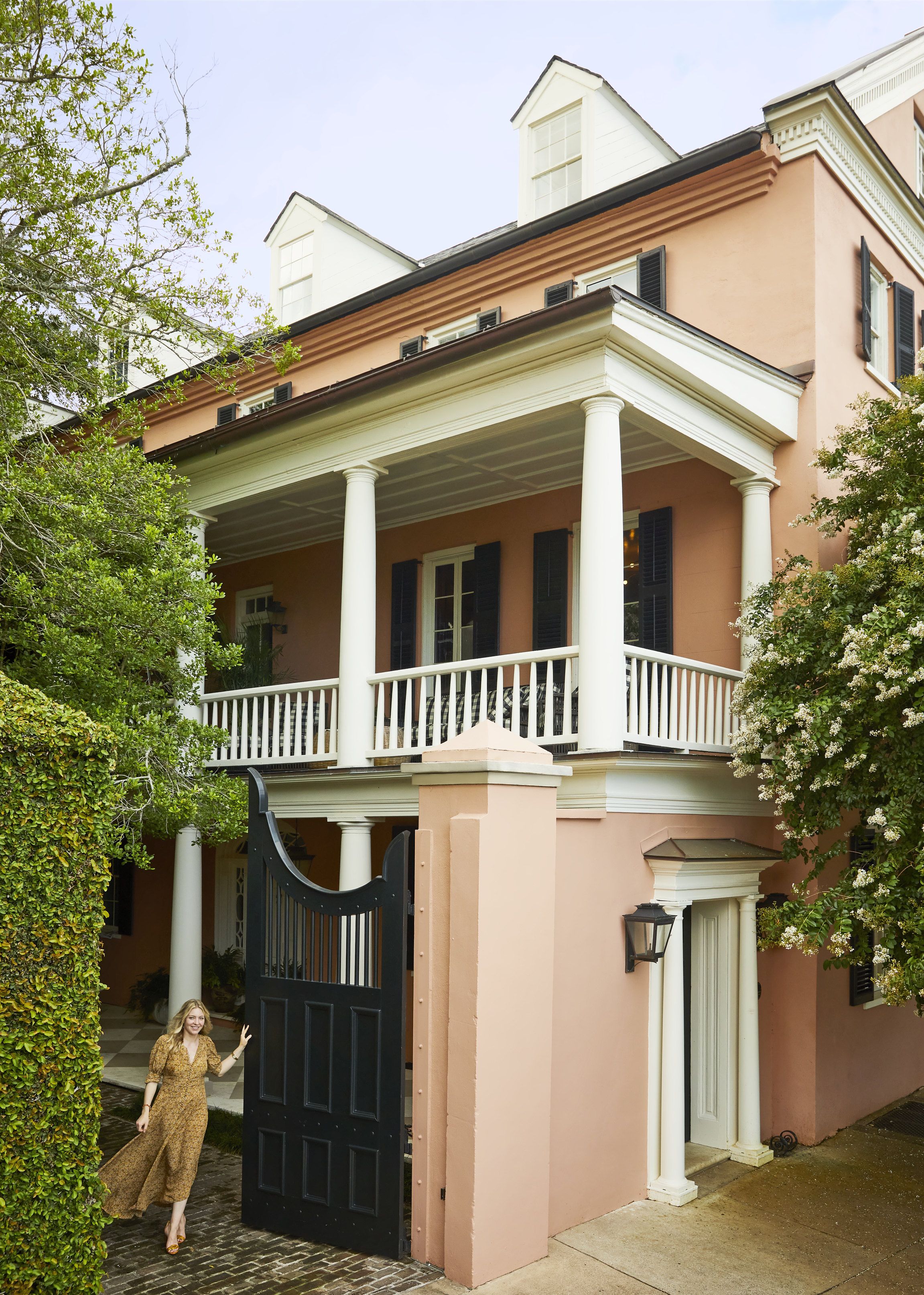 a three story peachy colored house with white columns and black shutters and gate