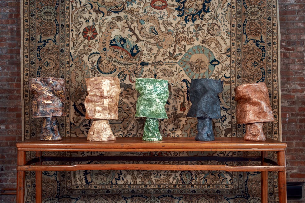 Display of five abstract sculptures on a wooden table against a patterned textile backdrop.