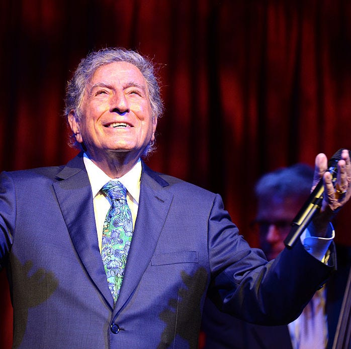 singer tony bennett pictured with a microphone in his hand while performing on stage, smiling looking up