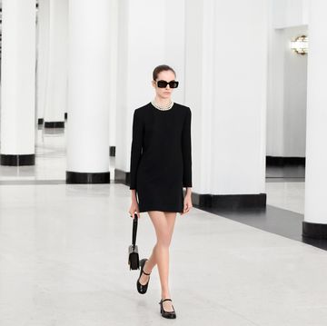 a man wearing a black dress and sunglasses walking in a large room