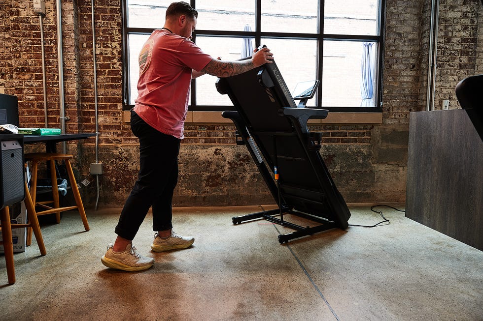 A person adjusting a folding treadmill in a workspace