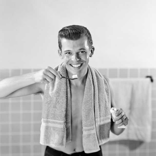 1950s smiling teenaged boy standing at bathroom sink brushing teeth looking at camera photo by cameriquegetty images