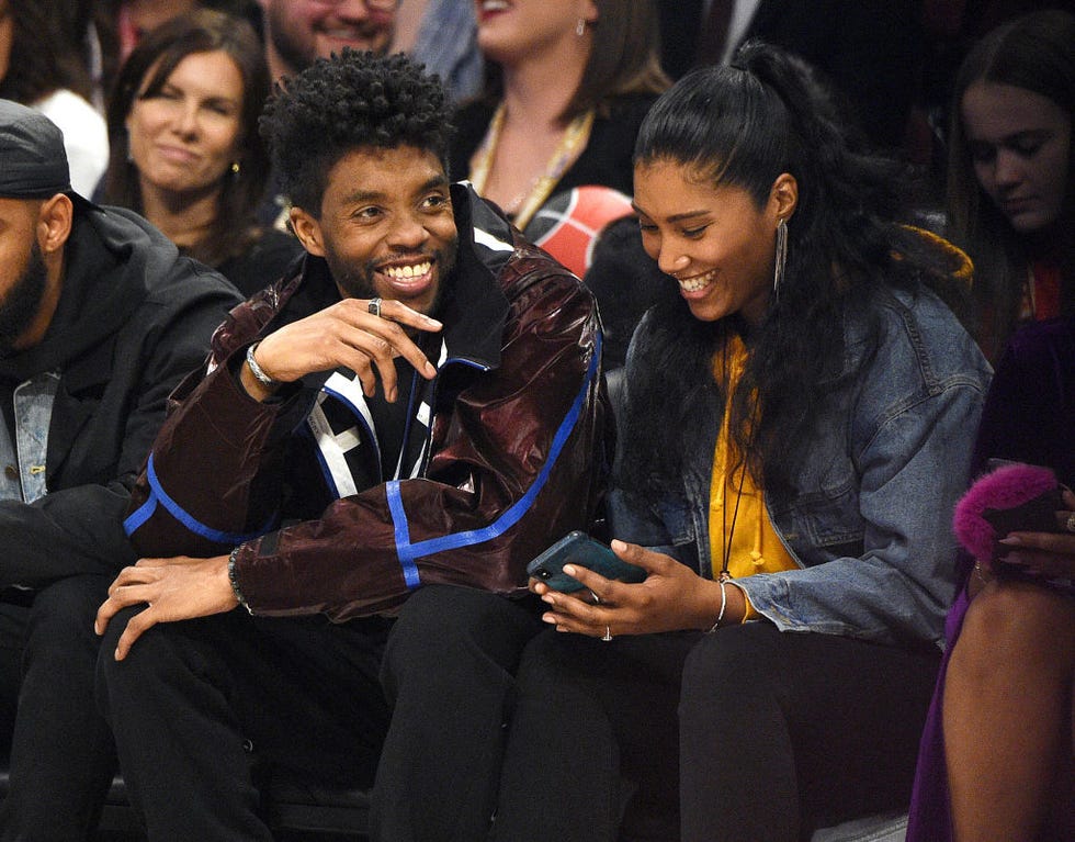 chadwick boseman and taylor simone ledward sit in a crowd and smile