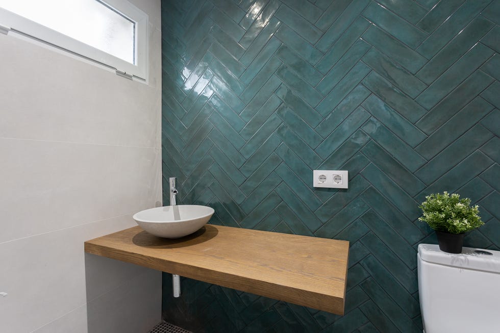 baño con azulejos azules en espiga y balda de madera flotante con el lavamanos