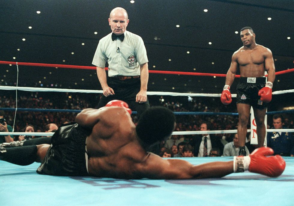 a boxing referee counting down a fighter on the canvas as mike tyson stands over them