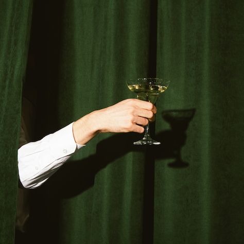 hand with a martini glass sticks out from the green curtains
