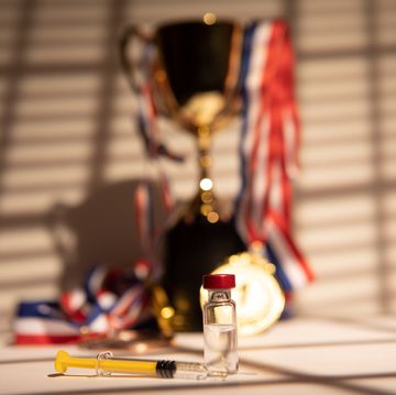 champion's cup and gold medals hanging with the light coming through the window, leaving the shadow of a blind at sunset, next to syringe with doping substance