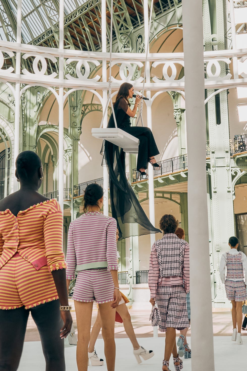 riley keough singing on a swing as models walk beneath her