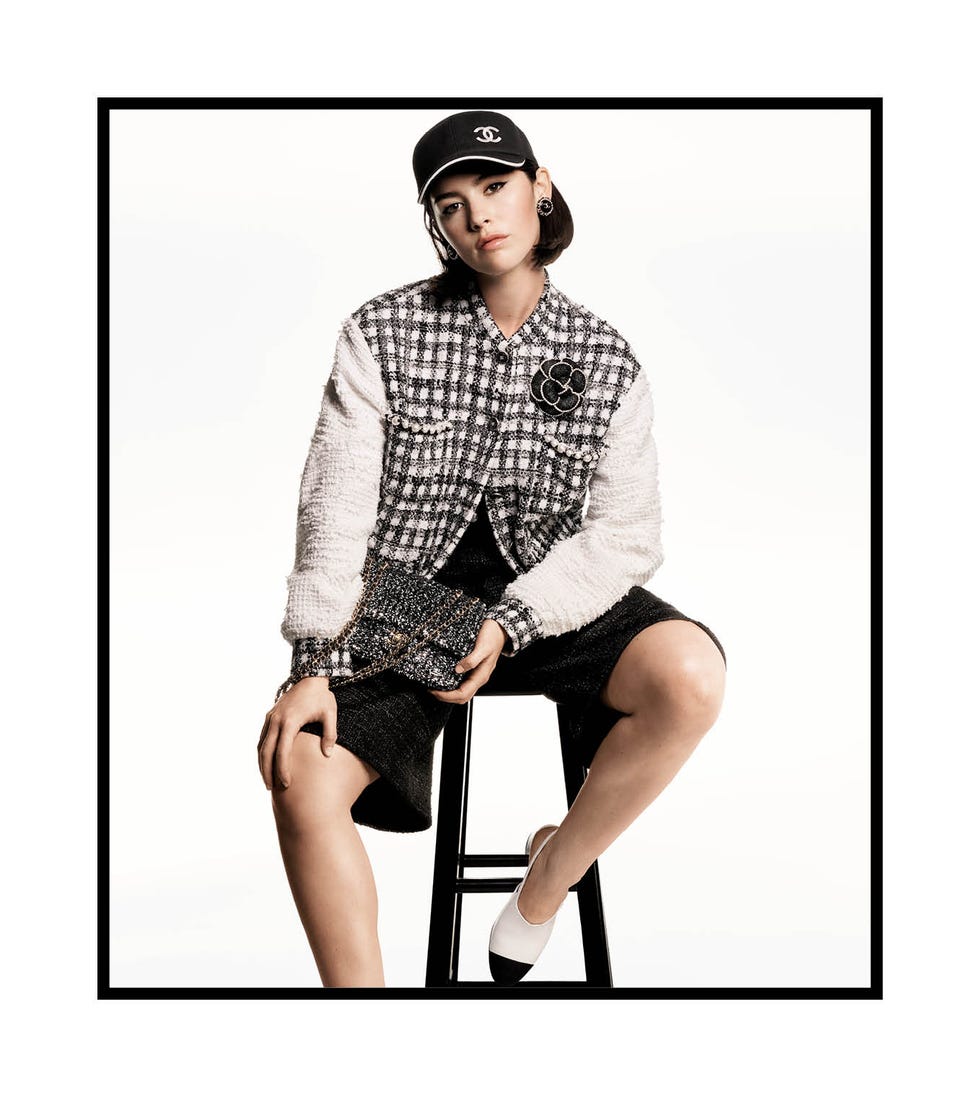 a brunette white woman wearing a stylish outfit with dark shorts a patterned top and baseball cap with chanel logo