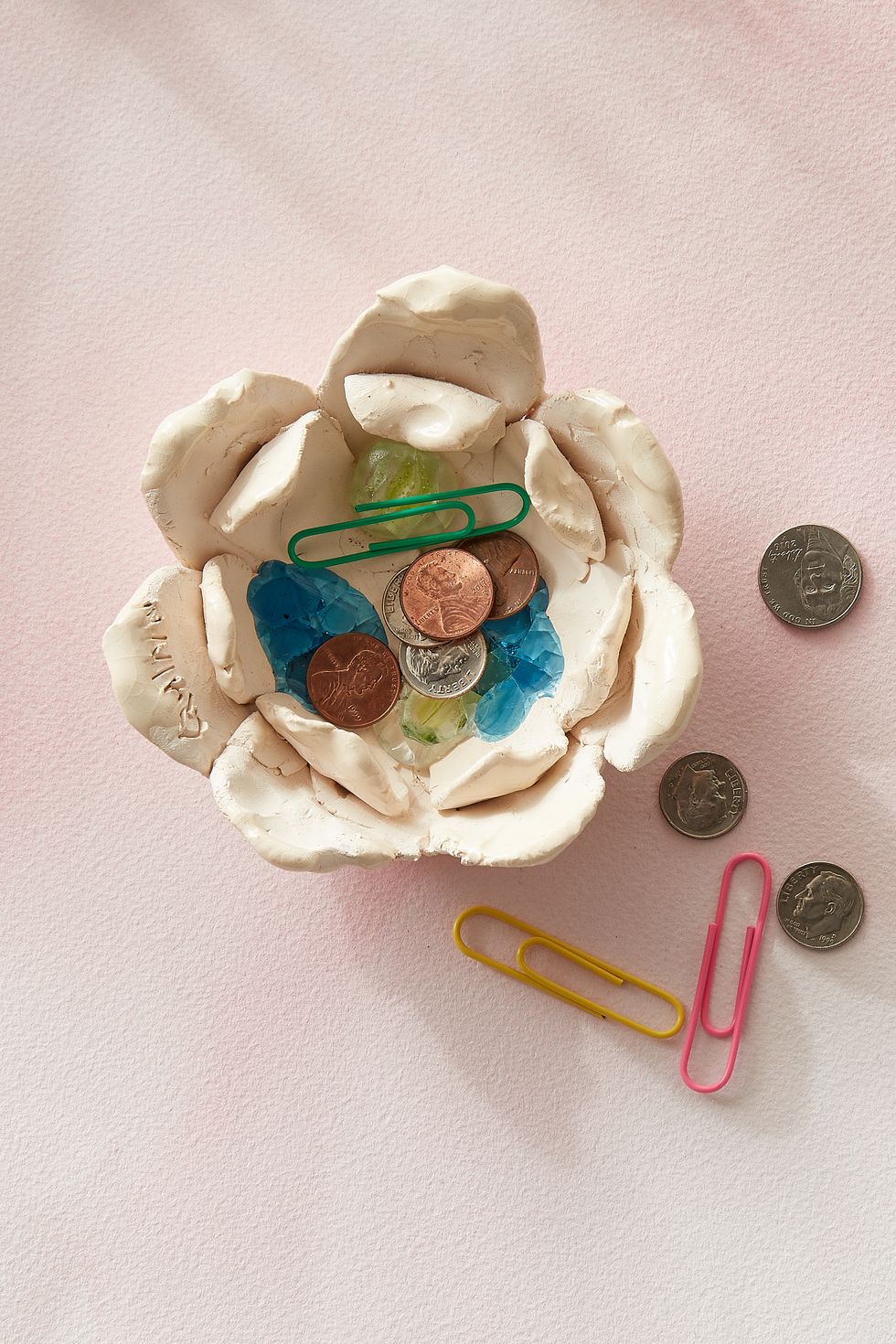 small flower shaped clay change bowl with child's signature inscribed in one petal holds dimes, pennies, and paper clips