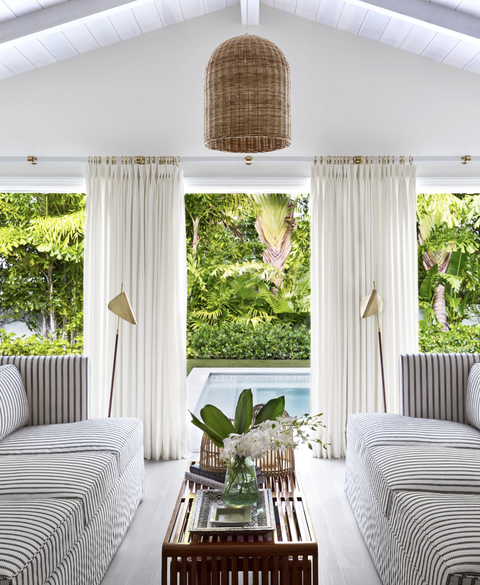 this palm tree beach bungalow designed by lindsey lane features coastal accents, like a rattan pendant lamp and side tables, for a warm and clean look