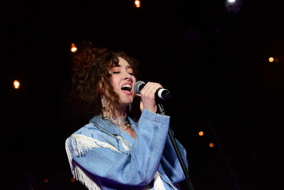 chappell roan sings into a microphone on a stand and wears a denim jacket with fringe