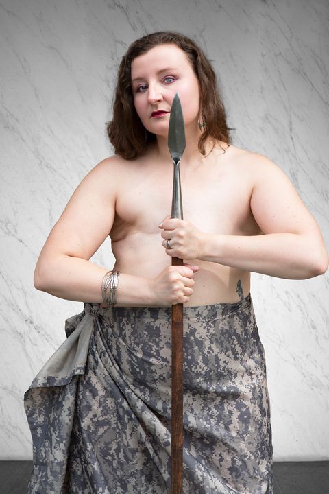 diana gerbehy holding a spear with no shirt and camo skirt she has had a double mastectomy