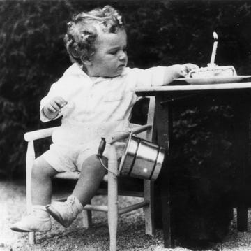 Charles Lindbergh Jr. on his first birthday charles lindbergh jr sits on a chair and reaches to a birthday cake with a lit candle to the right