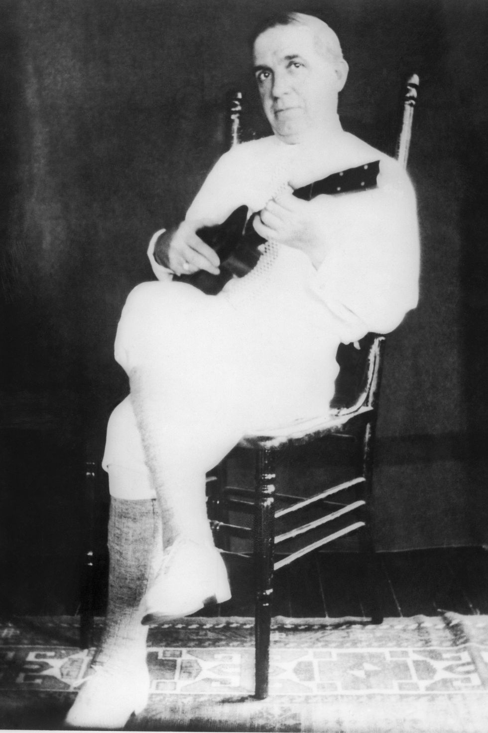 a man plays a ukulele while sitting in a chair and staring at the camera