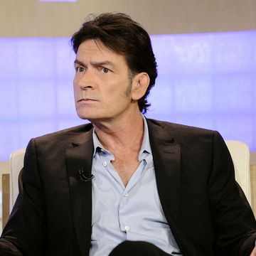 a man in a suit jacket and blue collared shirt sits in an armchair and looks to the left