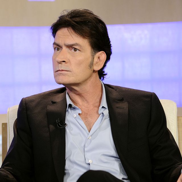 a man in a suit jacket and blue collared shirt sits in an armchair and looks to the left